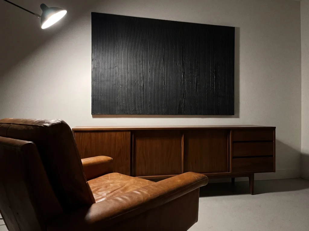 A large black plaster wall art piece with vertical ridges hangs above a credenza and leather armchair.