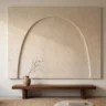 A simple japandi textured wall art panel with one asymmetrical sculpted arch in pale oatmeal plaster, above a low dark wood bench with a small ceramic vase