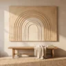 A textured arches canvas with concentric sculpted arches in warm sand and cream, hanging above a simple wooden bench in a bright, modest room