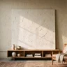 An oversized plaster canvas, taller than the console beneath it, with dramatic hand-troweled texture in off-white, leaning against a tall wall in a loft