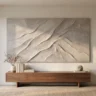 A wide abstract landscape plaster artwork with mountain-like ridges and soft grey-beige tones, hanging above a long low console