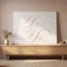 A crack-free modeling paste artwork with smooth, flowing raised swirls in white on canvas, leaning on a light oak console
