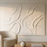 A bold sculptural plaster wall artwork with raised organic forms in warm white transforming a plain living room wall above a boucle armchair