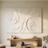 A sealed, crisp white sculpted plaster canvas with deep swirling texture hanging in a bright living room, its surface matte and clean