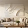 A smooth, crack-free white plaster relief artwork with flowing curves, hanging in a calm, bright living room above a linen sofa