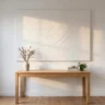 A minimalist white textured plaster canvas with gentle sweeping finger and trowel marks, hanging above a simple oak desk in a bright room