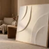 A high-end plaster artwork built on a plywood panel, the exposed plywood edge visible, with refined smooth curved relief in warm white, leaning on a console
