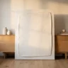A crisp, polished plaster art canvas with clean straight edges and confident sculpted texture in warm white, leaning on a light oak console