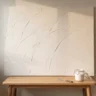 A finished textured canvas with soft sweeping trowel arcs in warm white hanging above a simple oak bench, with a palette knife and an open jar of white paste resting on the bench