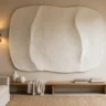 A plaster wall artwork styled in a designer living room, lit from the side by a brass sconce, with layered neutral decor