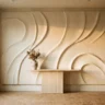 A luxe plaster wall artwork with large flowing relief curves in warm ivory, styled above a travertine console with a ceramic vase